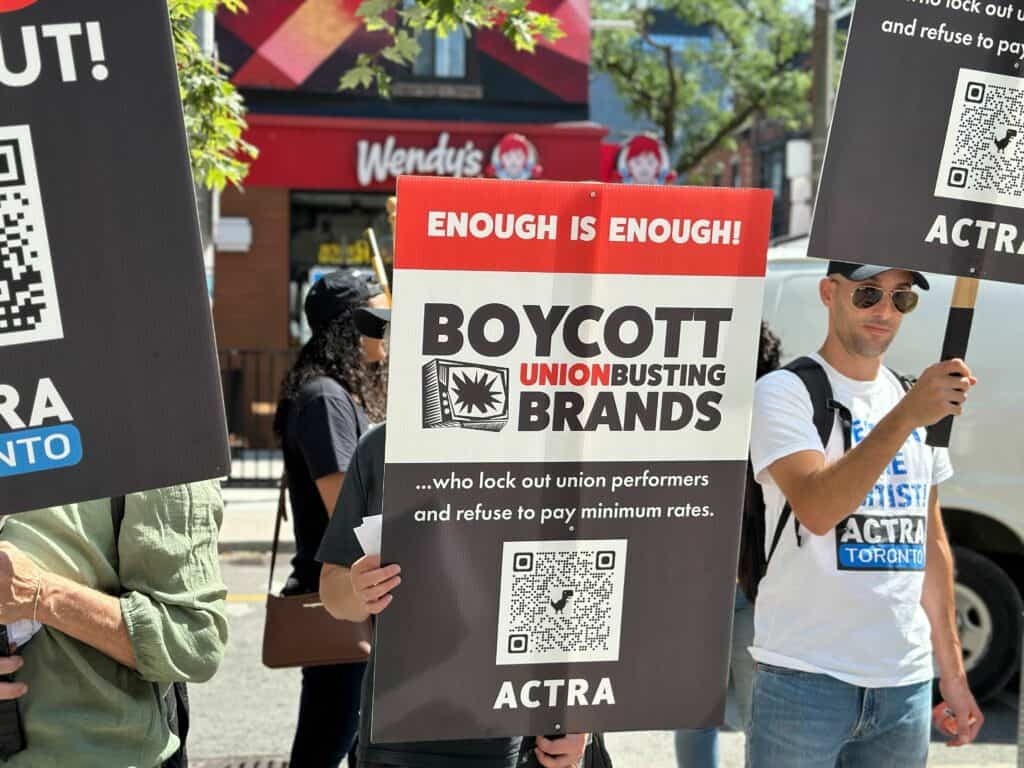 image of people holding up picket signs that read "enough is enough! boycott union busting brands... who lock out union performers and refuse to pay minimum rates." 