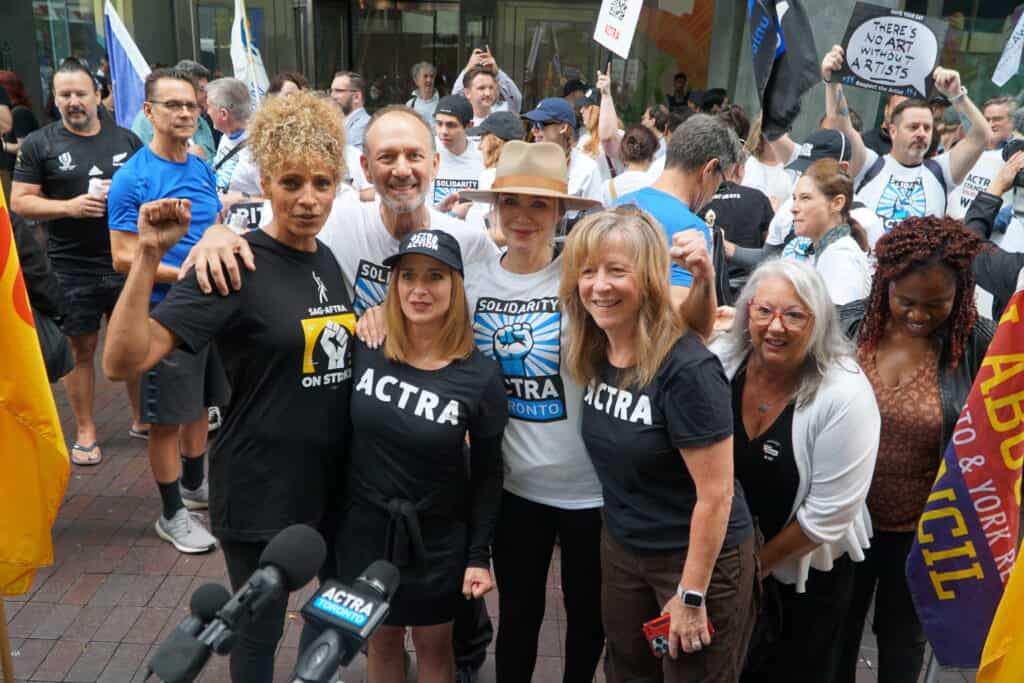 image of a large group of people at a rally , some with their fists raised in solidarity, others smiling and posing at the camera